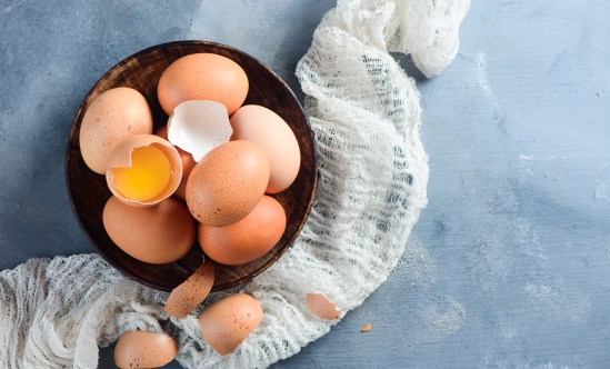 Fresh chicken eggs in a wooden bowl on a concrete background with white cloth. Organic ingredients concept with copy space.